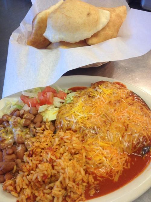 A plate of enchiladas topped with cheese, served with rice, refried beans, and a side of crispy tortillas in a basket.