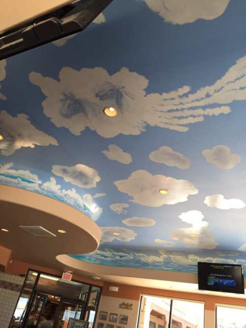 A painted ceiling depicting a blue sky with fluffy white clouds in a restaurant setting.