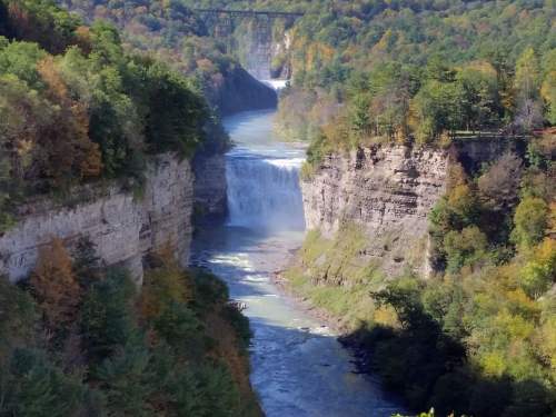 A scenic view of waterfalls cascading into a river, surrounded by lush green trees and rocky cliffs.