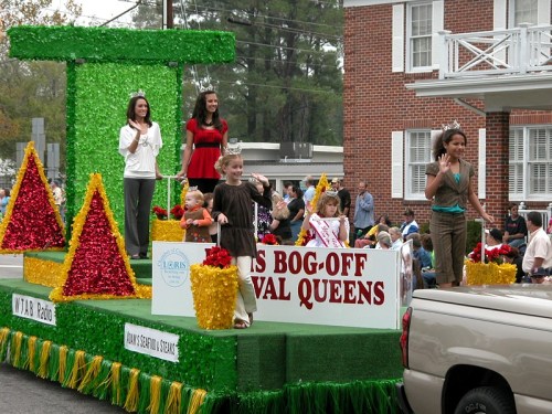 A colorful parade float featuring children and women in crowns, waving to the crowd during a festive event.