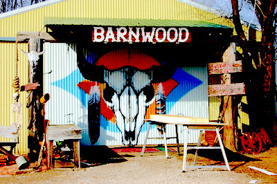 A rustic barn entrance with a painted bull skull and colorful designs, featuring wooden signs and outdoor furniture.
