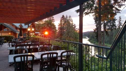 A scenic outdoor dining area with tables overlooking a river and trees at sunset.