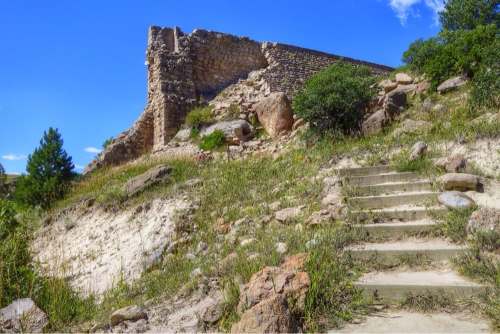 Ruins of a stone structure on a grassy hillside, with stone steps leading up to it under a clear blue sky.