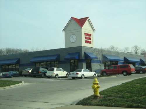 A large building with a clock tower, featuring blue awnings and a parking lot, surrounded by grass and a fire hydrant.