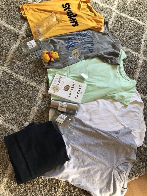 A flat lay of clothing items, including t-shirts, a white shirt, a green shirt, and two glasses, with a rubber duck and a book.