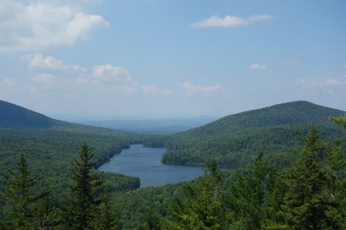 A serene landscape featuring a lake surrounded by lush green mountains under a clear blue sky.