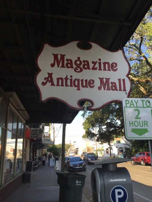 Sign for "Magazine Antique Mall" hanging above a sidewalk, with parking meter and street visible in the background.