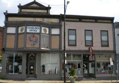 Two vintage shops with large windows and unique signage, showcasing clothing and accessories in a historic building.