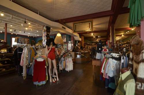 A vintage clothing store interior with racks of clothes, mannequins, and colorful decor.