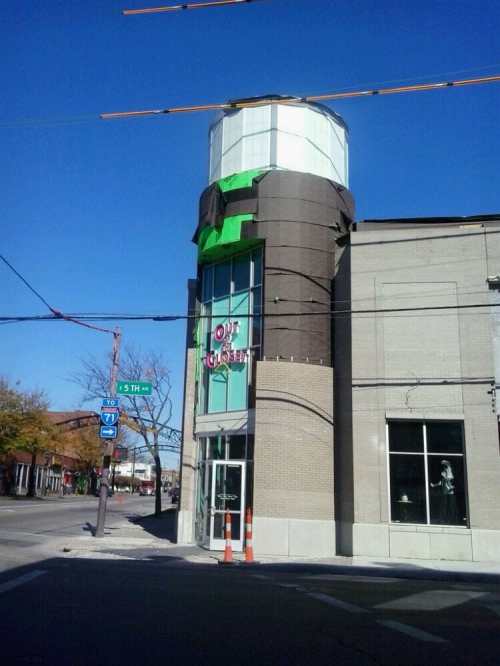 A modern building with a cylindrical tower, featuring a sign that reads "OUT" and "CLOSET," against a clear blue sky.