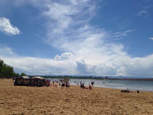 A sunny beach scene with people enjoying the water, sandy shore, and fluffy clouds in a blue sky.
