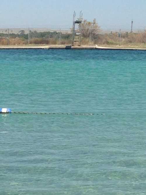 A calm body of water with a distant diving platform and a clear blue sky.