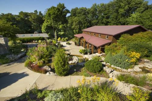 A scenic garden with a winding path, lush greenery, and a rustic building surrounded by vibrant flowers and trees.