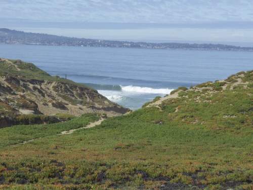 A serene coastal landscape with rolling green hills, gentle waves, and a calm ocean under a cloudy sky.