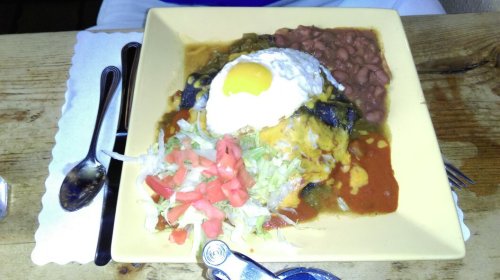 A plate of enchiladas topped with a fried egg, served with refried beans, lettuce, and diced tomatoes.