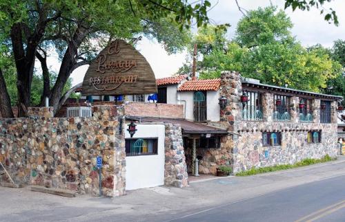 A rustic stone building with a wooden sign, surrounded by trees, along a quiet road.