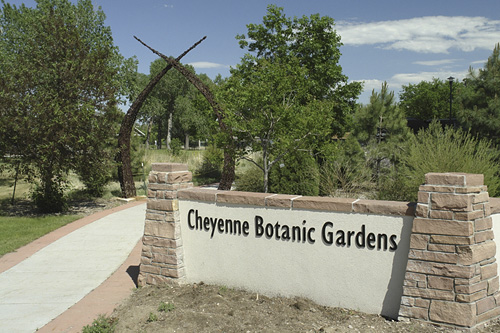 Sign for Cheyenne Botanic Gardens with a pathway and greenery in the background under a clear blue sky.