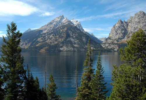 A serene lake surrounded by tall trees and majestic mountains under a clear blue sky.
