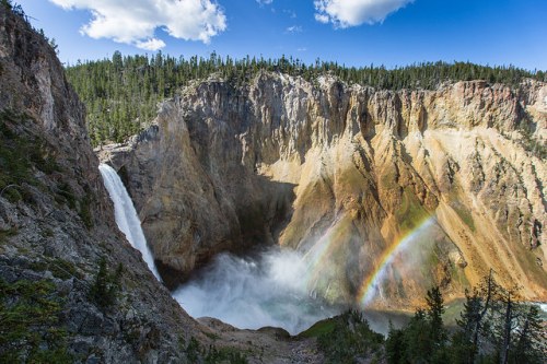 A stunning waterfall cascades into a canyon, with a vibrant rainbow arcing over the mist in a lush, green landscape.