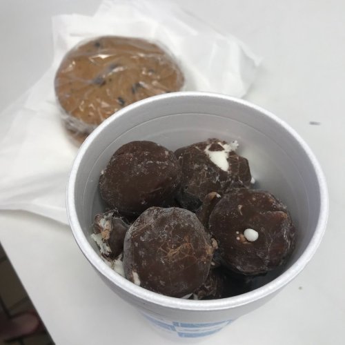 A cup filled with chocolate-covered treats, with a cookie wrapped in paper in the background.