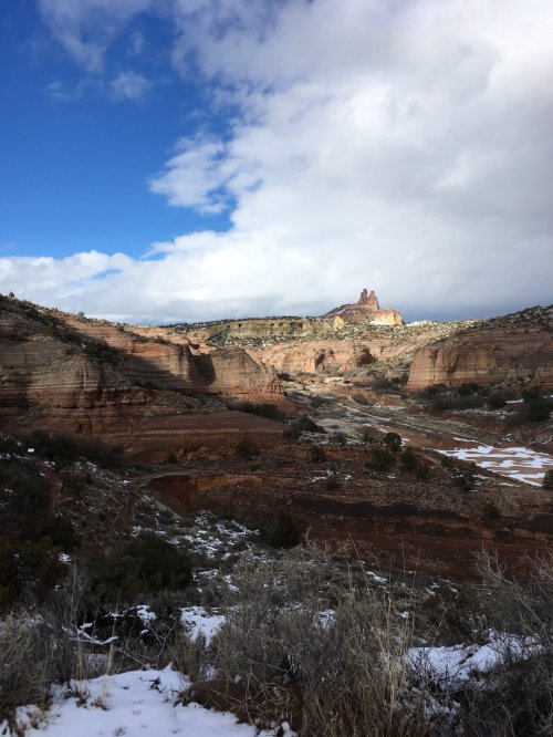 A scenic view of rugged red rock formations under a partly cloudy sky, with patches of snow on the ground.