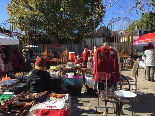 A bustling outdoor market with various stalls selling vintage items, clothing, and accessories under a clear blue sky.