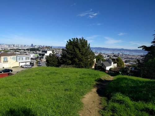 A grassy hilltop overlooking a city skyline and bay under a clear blue sky.