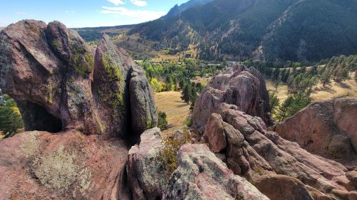 Rocky landscape with rugged formations, green valley, and mountains under a clear blue sky.