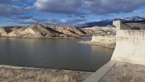 A serene landscape featuring a calm body of water surrounded by sandy hills and distant mountains under a cloudy sky.