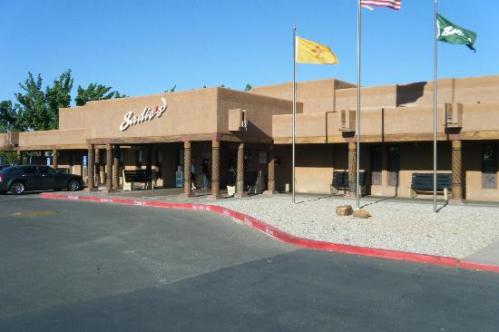 Exterior view of a southwestern-style building with flags and a parking lot. Clear blue sky in the background.