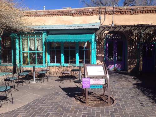 Colorful adobe building with turquoise accents, outdoor seating, and a sign in front. Bright, sunny day.