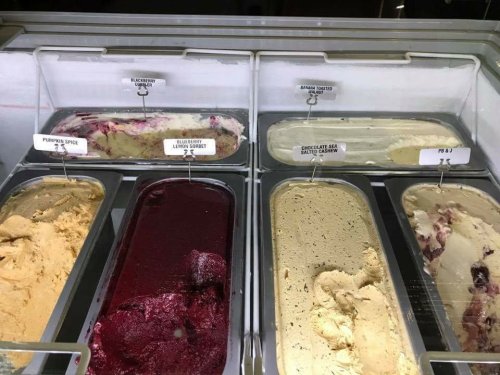 A display of various ice cream flavors in metal tubs, labeled with names like Pumpkin Spice and Chocolate Sea Salt Caramel.