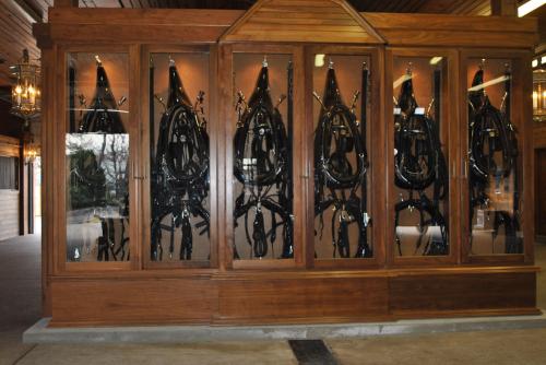 A wooden display case showcasing several black horse bridles in a stable setting.