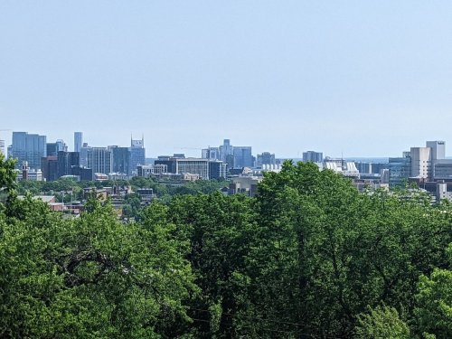 A city skyline with modern buildings and greenery in the foreground under a clear sky.