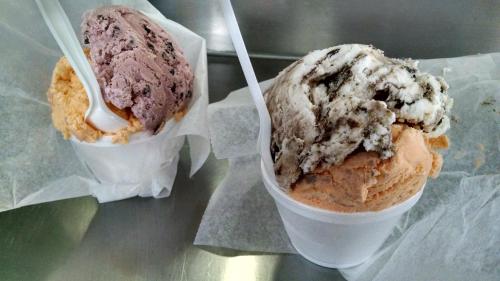 Two cups of ice cream: one with pinkish-purple and the other with orange and chocolate swirl, both on white paper.