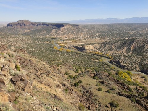 A panoramic view of a river winding through a rocky landscape with distant mountains under a clear blue sky.