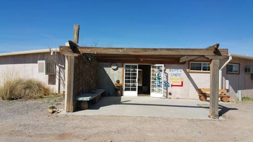 A rustic building entrance with a wooden awning, featuring glass doors and a simple concrete pathway.