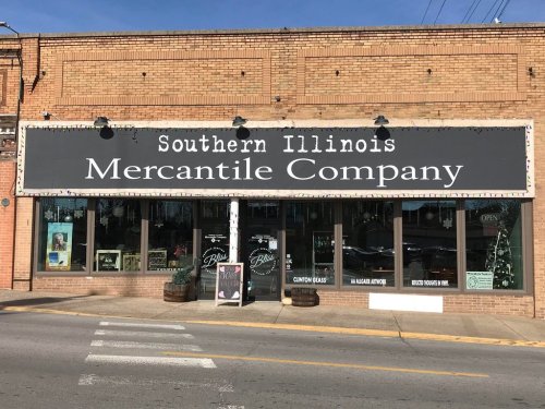 Sign for Southern Illinois Mercantile Company on a brick storefront, featuring large windows and festive decorations.