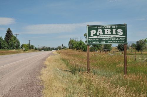 Sign welcoming visitors to Paris, established in 1863, with details on elevation and population, alongside a rural road.