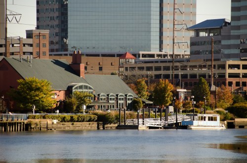 A riverside view featuring a green-roofed building, trees with autumn colors, and modern city buildings in the background.
