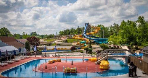 A vibrant water park featuring a large pool, colorful water slides, and lounge chairs under a partly cloudy sky.