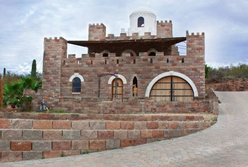 A stone castle-like building with arched doors and a dome, surrounded by a landscaped area and a paved pathway.