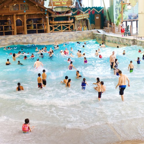 A lively indoor water park with children and adults enjoying the wave pool and water attractions.