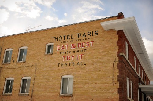 A brick building with a sign reading "Hôtel Paris" and advertisements for dining and lodging services.