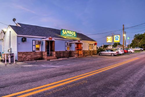 A restaurant named "Sambo's" at dusk, featuring a sign and parked cars along a quiet street.