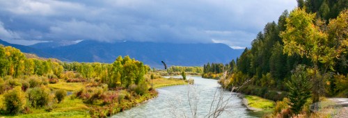 A winding river flows through a lush landscape of trees and mountains under a cloudy sky.