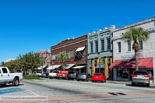 A street view featuring historic buildings, parked cars, and palm trees under a clear blue sky.