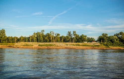 A serene river scene with trees lining the shore under a clear blue sky.