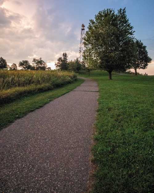 A winding path through a grassy area, leading to a tower in the distance under a cloudy sky.