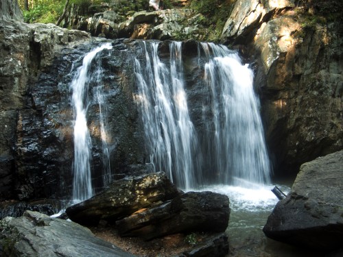 A serene waterfall cascading over rocky terrain, surrounded by lush greenery and a tranquil pool below.